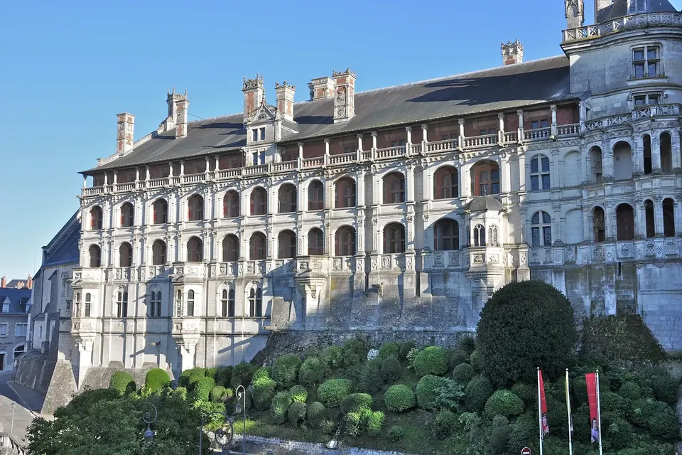 Longue façade Renaissance à arcades sur plusieurs étages, au-dessus de jardins taillés, sous un ciel bleu