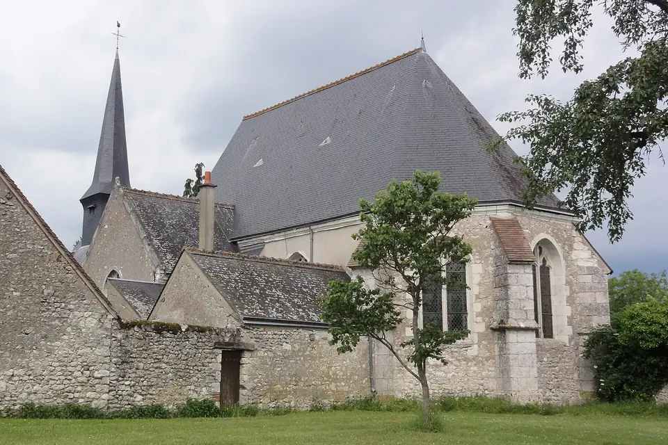 Église de village au toit d'ardoise et au clocher pointu, entourée d'un mur de pierre et de jardins