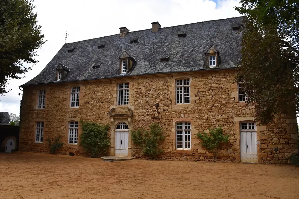 Grande maison de pierre aux toits de lauzes et pelouses d'un jardin à la française