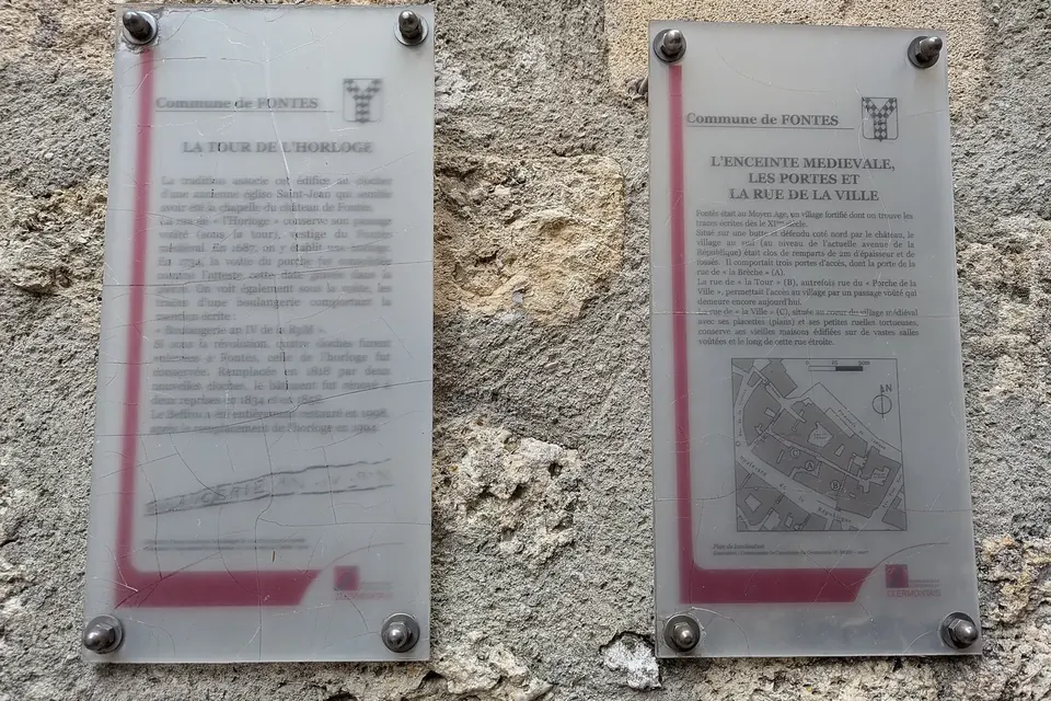 Deux panneaux d'information patrimoniale fixés sur un mur de pierre, avec textes et plan de la ville