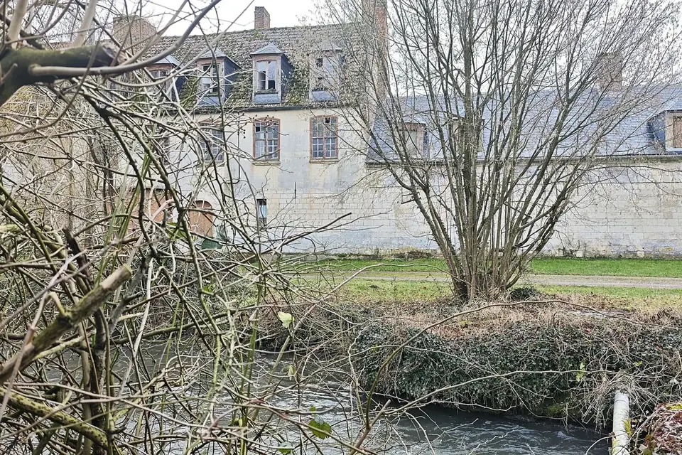 Façade d'un ancien manoir seigneurial vu à travers les branches, au bord d'une rivière