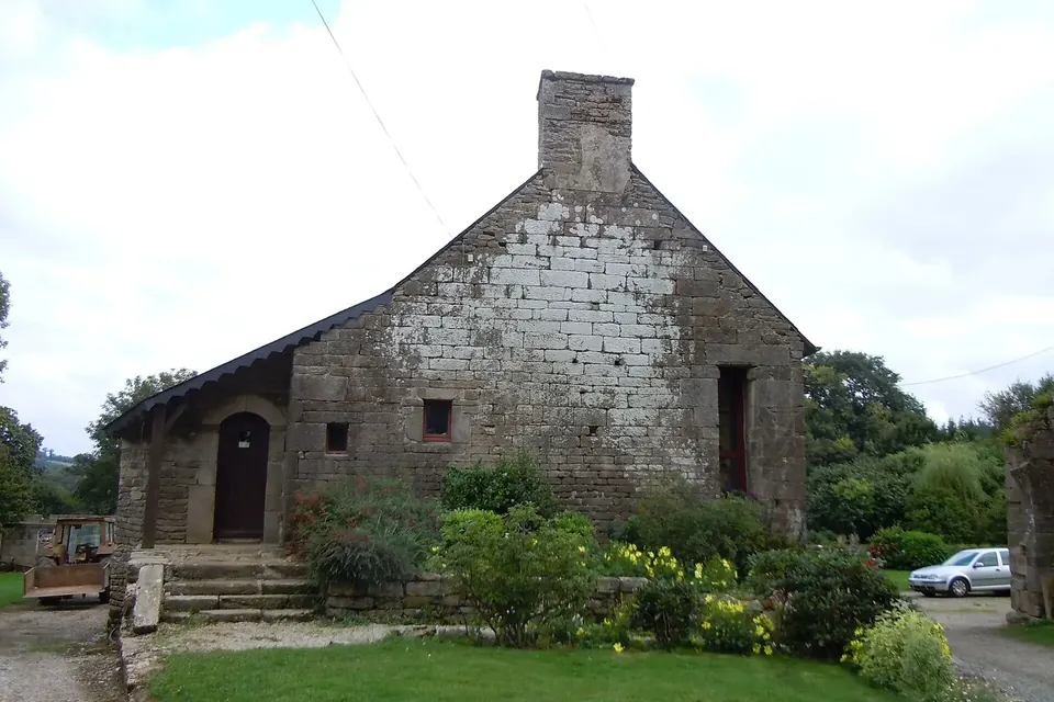 Pignon de manoir breton en pierre de taille avec cheminée et porte en arc, entouré de jardins