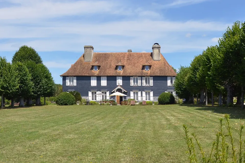Manoir à deux étages au toit de tuiles, au fond d'une grande pelouse bordée d'arbres taillés
