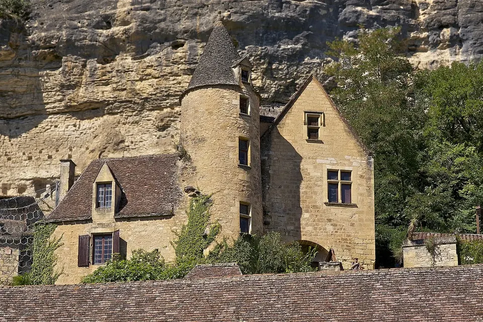 Maison ancienne en pierre blonde avec tour ronde, adossée à une falaise à La Roque-Gageac
